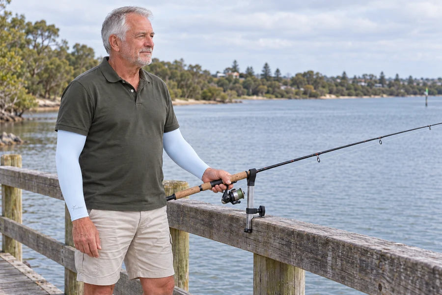 Man in light blue IceRays arm sleeves holding a fishing rod beside a jetty rail.